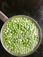 Pot of peas and broadens cooking on a stove top. Black stove top with copy space.  Cooking at home; no people.