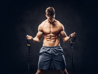 Fototapeta premium Handsome shirtless man with stylish hair and muscular ectomorph doing the exercises with an expander.