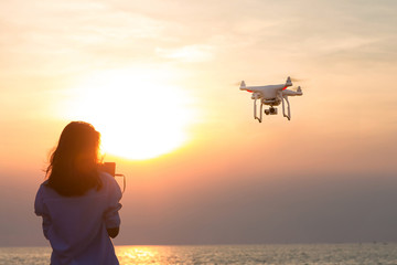 Silhouette of young woman using drone at sunset for photos and video making - Happy woman having...