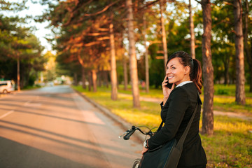 Fototapeta na wymiar Smiling young woman talking on the phone while riding a bike.