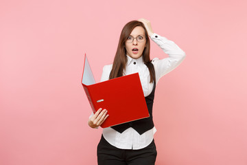 Young shocked business woman in glasses holding red folder for papers document clinging to head isolated on pastel pink background. Lady boss. Achievement career wealth. Copy space for advertisement.