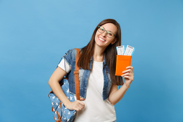 Portrait of young joyful woman student in glasses with backpack holding passport, boarding pass tickets isolated on blue background. Education in university college abroad. Air travel flight concept.