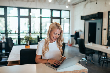 Beautiful woman working on laptop in modern open-space office.