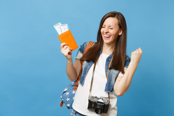 Young overjoyed woman student with retro vintage photo camera holding passport, boarding pass tickets doing winner gesture isolated on blue background. Education in college abroad. Air travel flight.