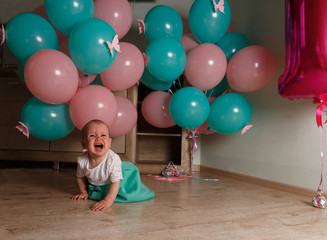 Fototapeta na wymiar the child cries, gets angry, a little girl, a child, sits on the floor and cries, wrinkled her nose, near the balloons, a holiday. birthday, turned a year old. resentment, disappointment