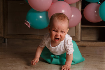 Obraz premium the child cries, gets angry, a little girl, a child, sits on the floor and cries, wrinkled her nose, near the balloons, a holiday. birthday, turned a year old. resentment, disappointment
