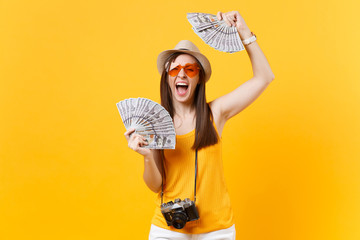 Tourist woman in summer casual clothes, hat holding bundle lots of dollars, cash money isolated on yellow orange background. Female traveling abroad to travel on weekends getaway. Air flight concept.