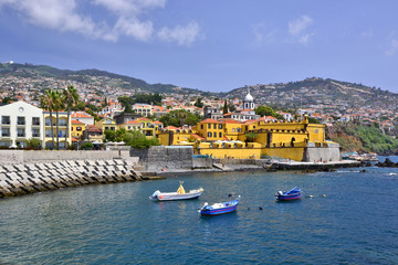 Fototapeta na wymiar Fishing boats, city beach and ancient fortress Sao Tiago Fort on the coast by the port of Funchal in Madeira island, Portugal