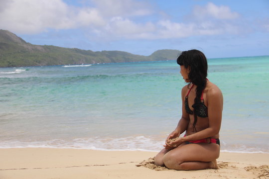 H&uuml;bsche Frau mit Strand-Bikini sitzt am Strand im Hintergrund das karibische Meer, Berge und Himmel.