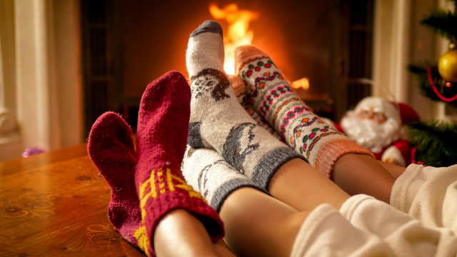 Closeup image of parents and childs feet in warm woolen socks lying next to burning fireplace