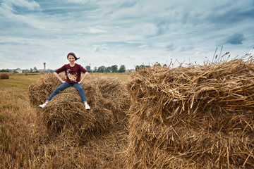 Naklejka na ściany i meble young girl having fun in the field, sitting on a haystack