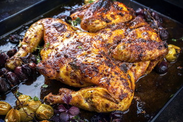 Modern style spatchcocked barbecue chicken al mattone chili with red and green grapes as top view on an old metal sheet