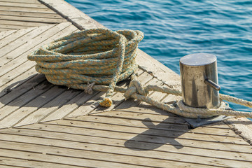 Mooring rope and bollard on sea water and yachts background.