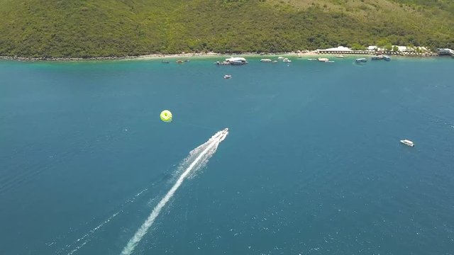 Parasailing in blue sea bay drone view. Aerial view sailing boat with paragliding in turquoise sea. Beautiful landscape blue lagoon and resort beach on island.