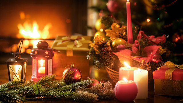 Closeup image of traditional Christmas decorations and candles on wooden table against fireplace