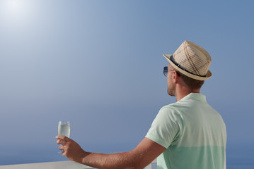 Man traveler relaxing on resort balcony with glass of sparkling wine against sea.