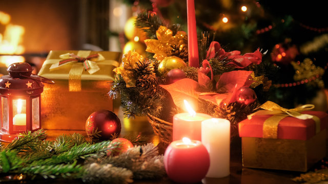 Closeup image of burning candles in traditional wreath against Christmas tree and fireplace