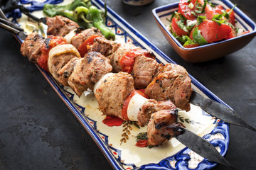 Traditional Greek souvlaki barbecue skewer with  tomato onion salad and paprika as closeup on a plate