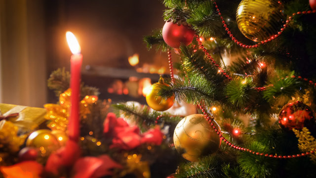 Closeup image of decorated Christmas tree branch against burning candle on traditional wreath