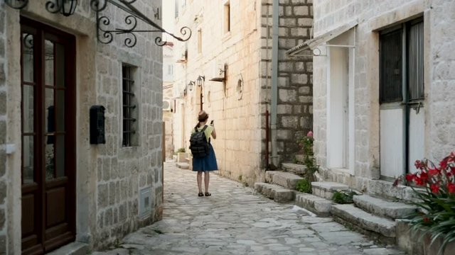 Young happy woman traveling at Montenegro and looking Perast landmarks, hipster girl with map at the city center make a photo. Vacation and travel concept.