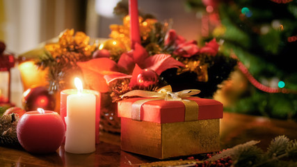 Fototapeta na wymiar Closeup photo of candles and gifts on wooden table against Christmas tree