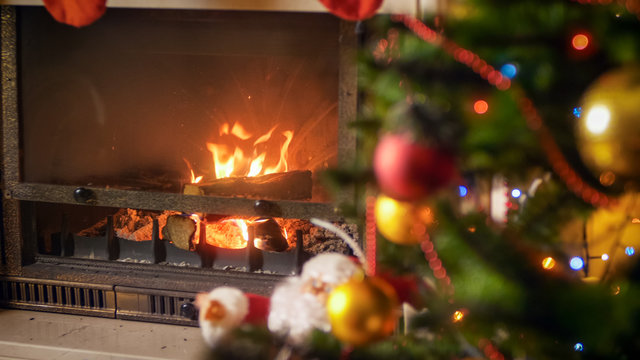Closeup image of burning fireplace next to decorated Christmas tree