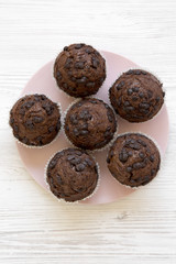 Tasty chocolate muffins on pink plate on white wooden table, top view. Overhead, from above.