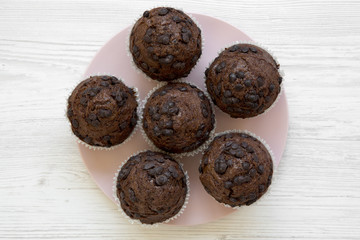 Delicious chocolate muffins on pink plate on white wooden surface, top view. Flat lay, overhead, from above.