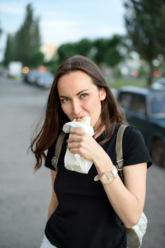 Young woman bites Shawarma on the street, quick snack, street food on the go