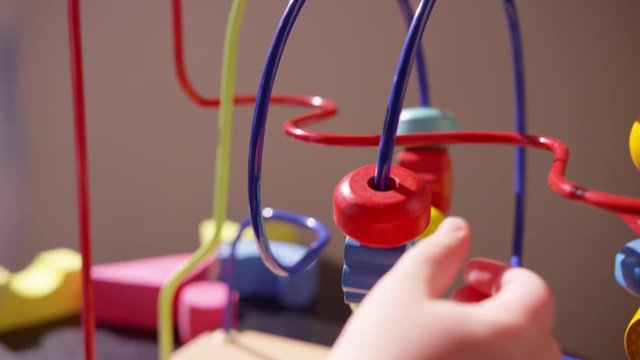 Close view of toddler's hand pushing several beads along a rollercoaster toy