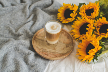 Cup with hot cappuccino, gray pastel woolen blanket, sunflowers, bedroom, morning concept