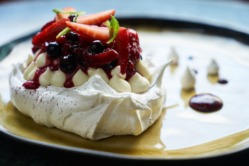 Pavlova meringue cake with fresh berries and custard cream on plate on green marble table background, close-up 