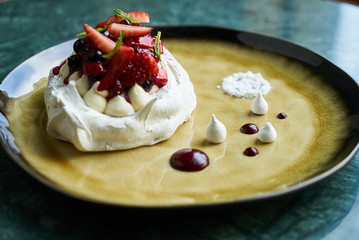 Pavlova meringue cake with fresh berries and custard cream on plate on green marble table background, close-up 