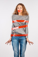 Scared young woman wrapped in red tape over white background