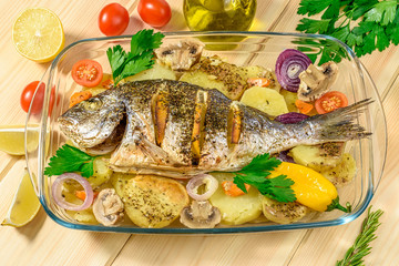 Baked sea bream with lemon, onions, herbs, cherry tomatoes, spices and baked potatoes on a wooden background. Fried tasty fish. Diet and healthy food.