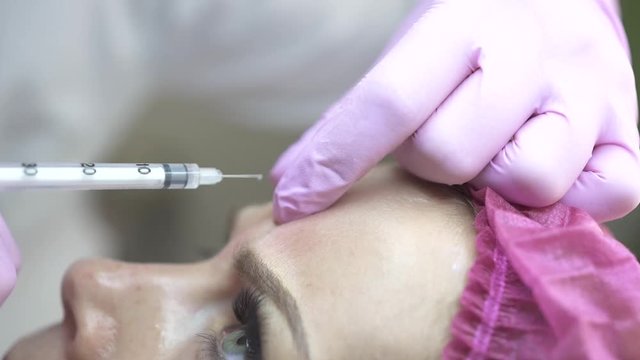 Face woman getting beauty injection in cosmetic clinic. Close up cosmetologist doing botox injection in forehead to patient in beauty clinic. Rejuvenation, injectable cosmetology and medicine concept.