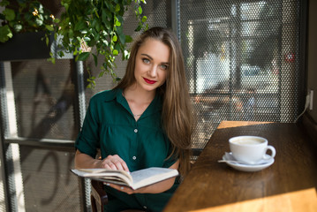 Young beautiful girl sitting at a cafe reading a book and drinking morning coffee