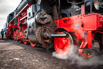 Naklejka premium Steamy and rolling old locomotive with red steel wheels on on-site shunting platform, authentic industrial details and craftsmanship along the rail way and train station