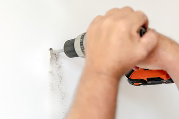 Close-up man holding power drill in hand and making hole in white wall. DIY. House building repair...
