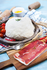 Dough for pizza with ingridients: cherry tomatoes, chili pepper and prosciutto on blue wooden table