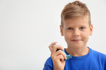 Little boy with asthma inhaler on light background