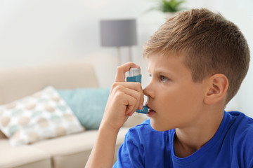 Little boy using asthma inhaler on blurred background