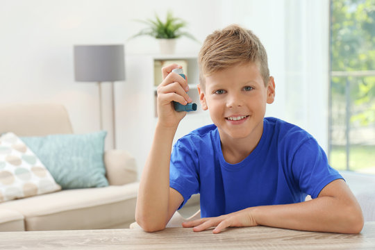 Little boy with asthma inhaler at table indoors