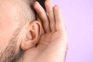 Fototapeta premium Young man with hearing problem on color background, closeup