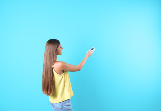 Young woman with air conditioner remote on color background, copy space text