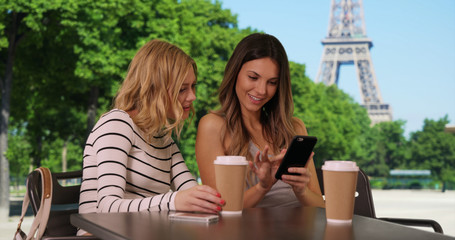 Two Cute white girls seated using mobile phone by Eiffel Tower