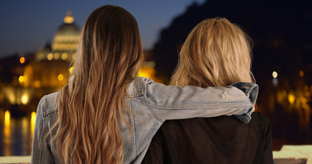 Young brunette with arm around blonde friend's shoulder in Rome, Italy