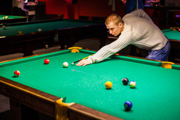 Fototapeta premium young handsome guy in a white sweater playing billiards