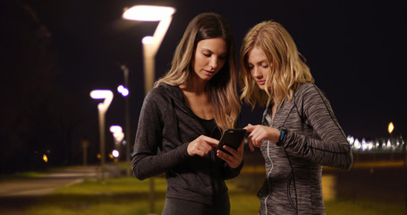 Two attractive women timing jog with stop watch and smartphone outside at night