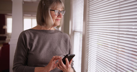 Lovely mature woman using smart phone device to send texts inside her home